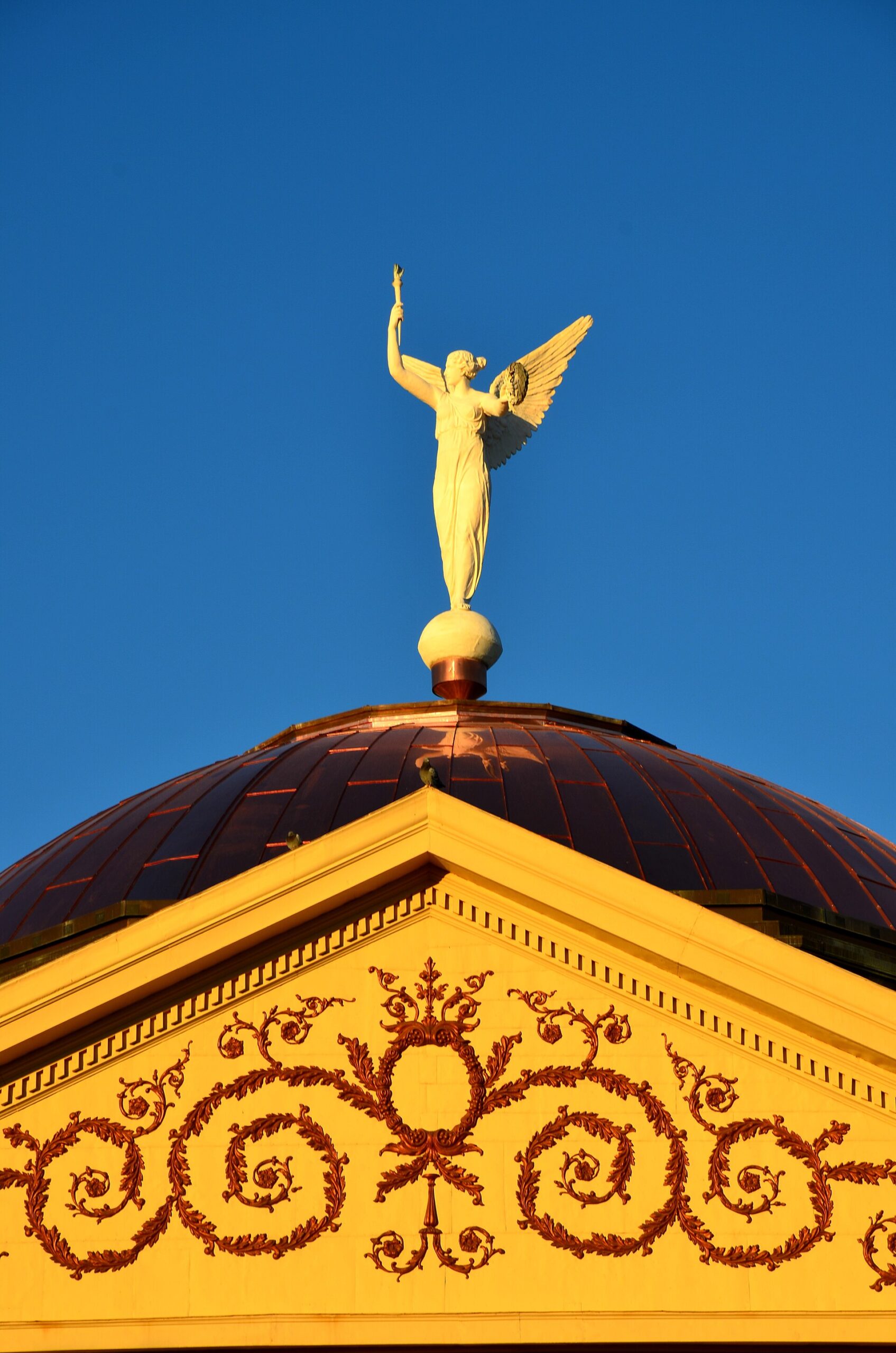 Winged Victory statue on the copper dome of the Arizona Capitol Museum against a blue sky