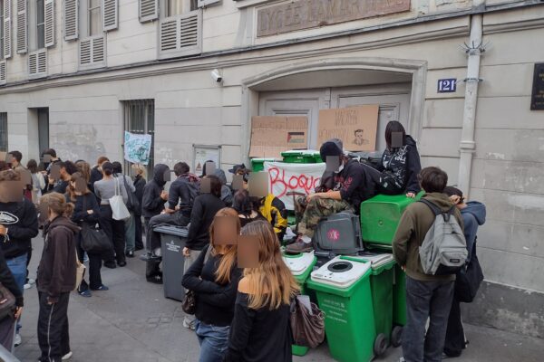 Teenage students gathered on a Paris sidewalk outside a blockaded high school entrance