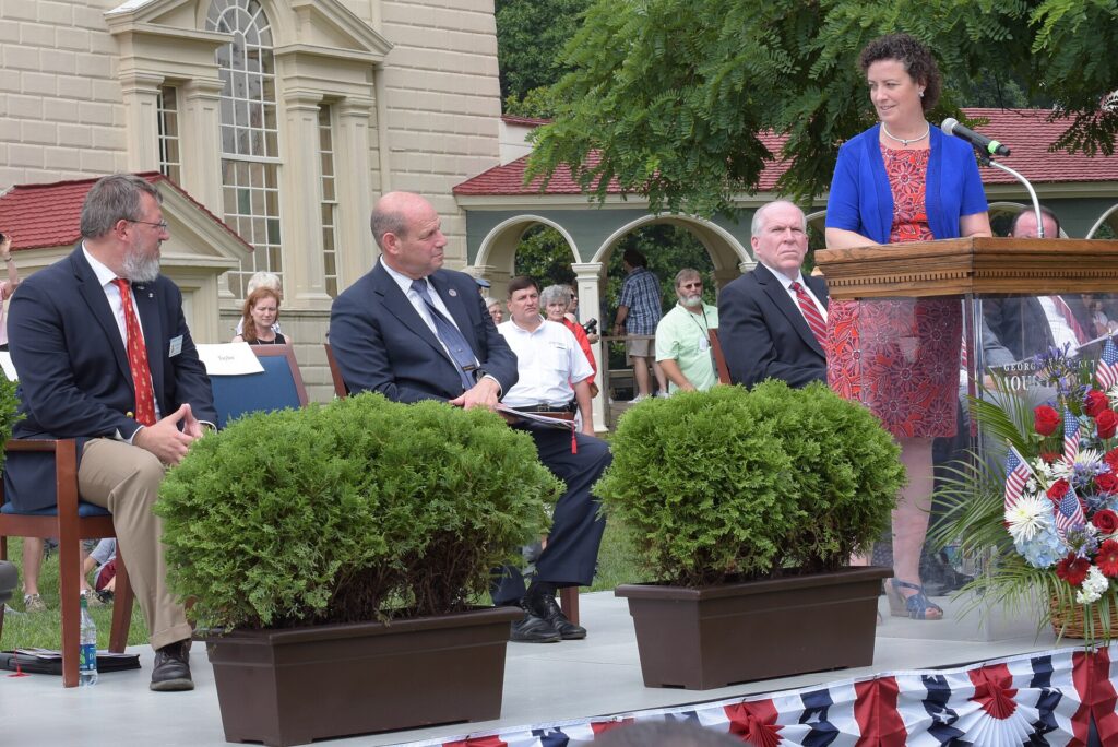 Officials on a stage with flags administering the citizenship oath at an outdoor ceremony