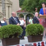 Officials on a stage with flags administering the citizenship oath at an outdoor ceremony