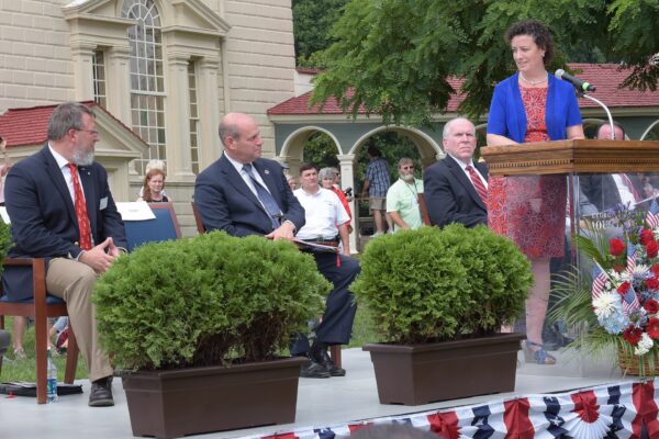 Officials on a stage with flags administering the citizenship oath at an outdoor ceremony
