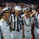NFL officials in striped shirts posing with Navy officers on a football field