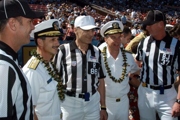 NFL officials in striped shirts posing with Navy officers on a football field