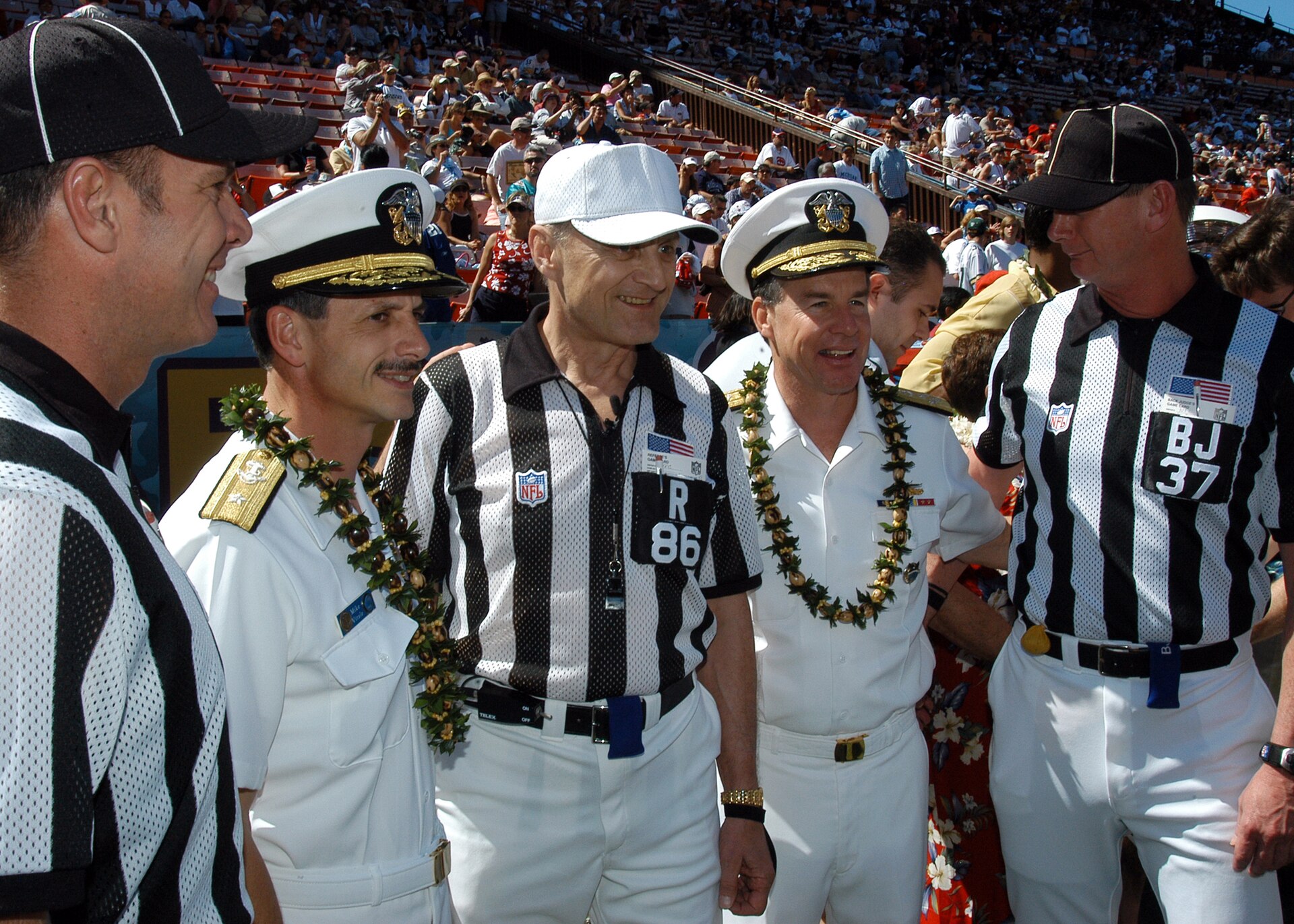 NFL officials in striped shirts posing with Navy officers on a football field