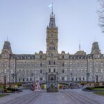 The ornate stone Parliament Building of Quebec with a central clock tower and autumn trees