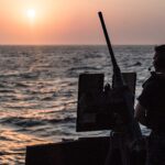 Silhouette of a sailor manning a deck gun at sunset over the Bab el-Mandeb Strait