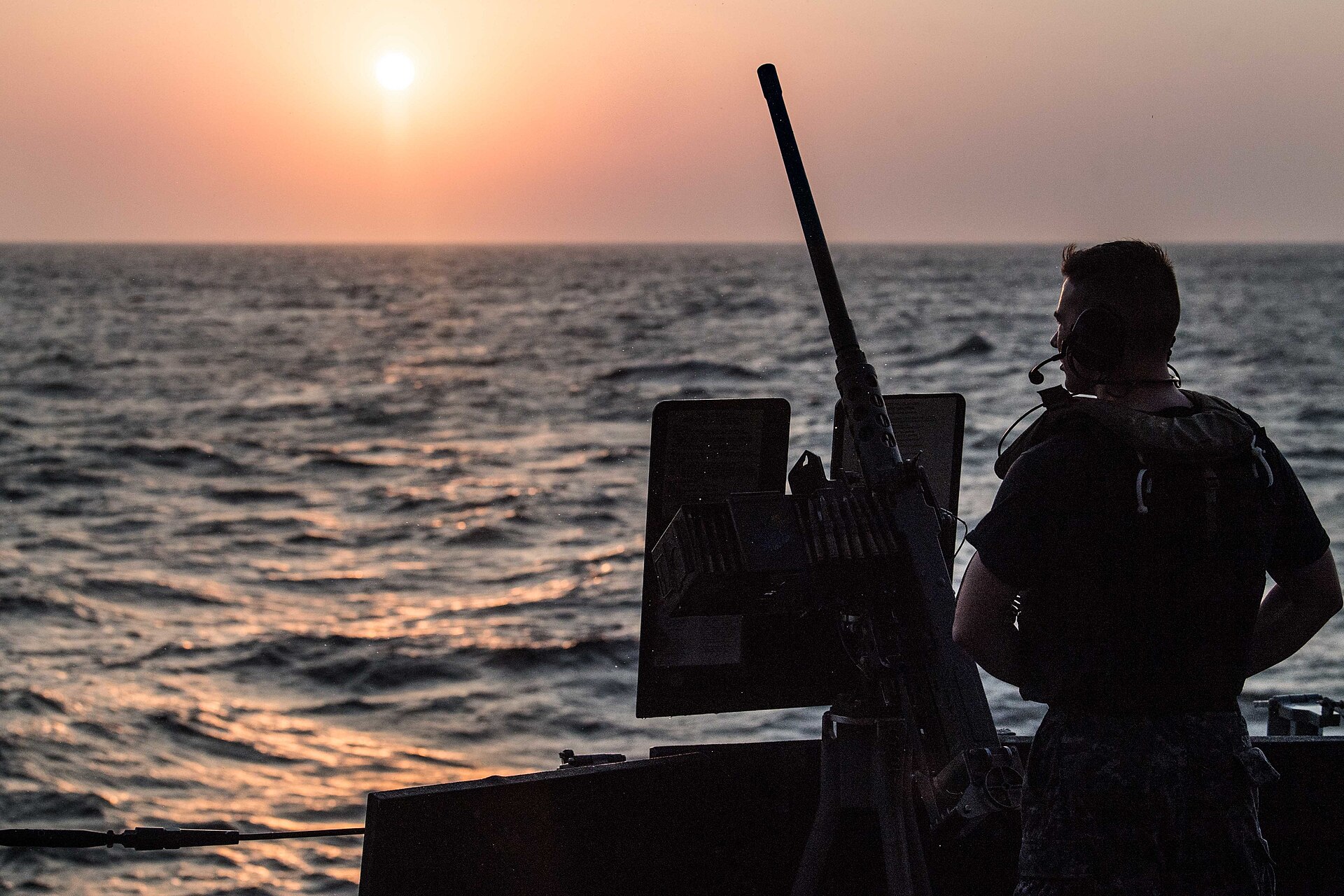Silhouette of a sailor manning a deck gun at sunset over the Bab el-Mandeb Strait
